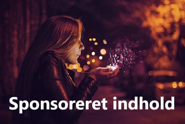 Kvinde blæser farverigt tryllestøv ud af sin hånd en mørk aften i gadelysenes skær